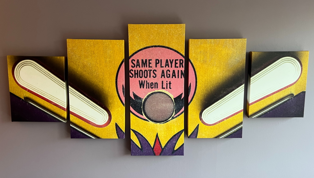 Five painted panels of pinball flippers on a wall, with a pink circle reading Same Player Shoots Again When Lit